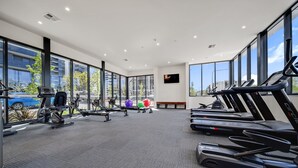 Une salle de sport moderne équipée de tapis de course, d’appareils de musculation et de ballons d’exercice. De grandes fenêtres offrent une vue sur l’extérieur.