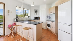 A modern kitchen with a large island, white cabinetry, and a view of the outdoors. - Oceanside Apartment With Views of Yaroomba Beach (Sunshine Coast)