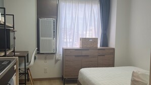 A bedroom with a bed, a dresser, a desk with a chair, a radiator, and a window with curtains.