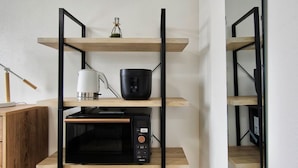 A kitchen with a microwave, kettle, and a small plant on a wooden shelf.