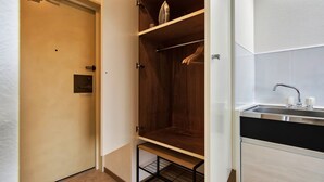 A compact room with a wooden closet, a built-in shelf, a small wire shelf, and a sink with a faucet.