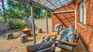 Un patio couvert avec un mur en briques, un foyer extérieur, du mobilier de jardin et une structure en forme de pergola.