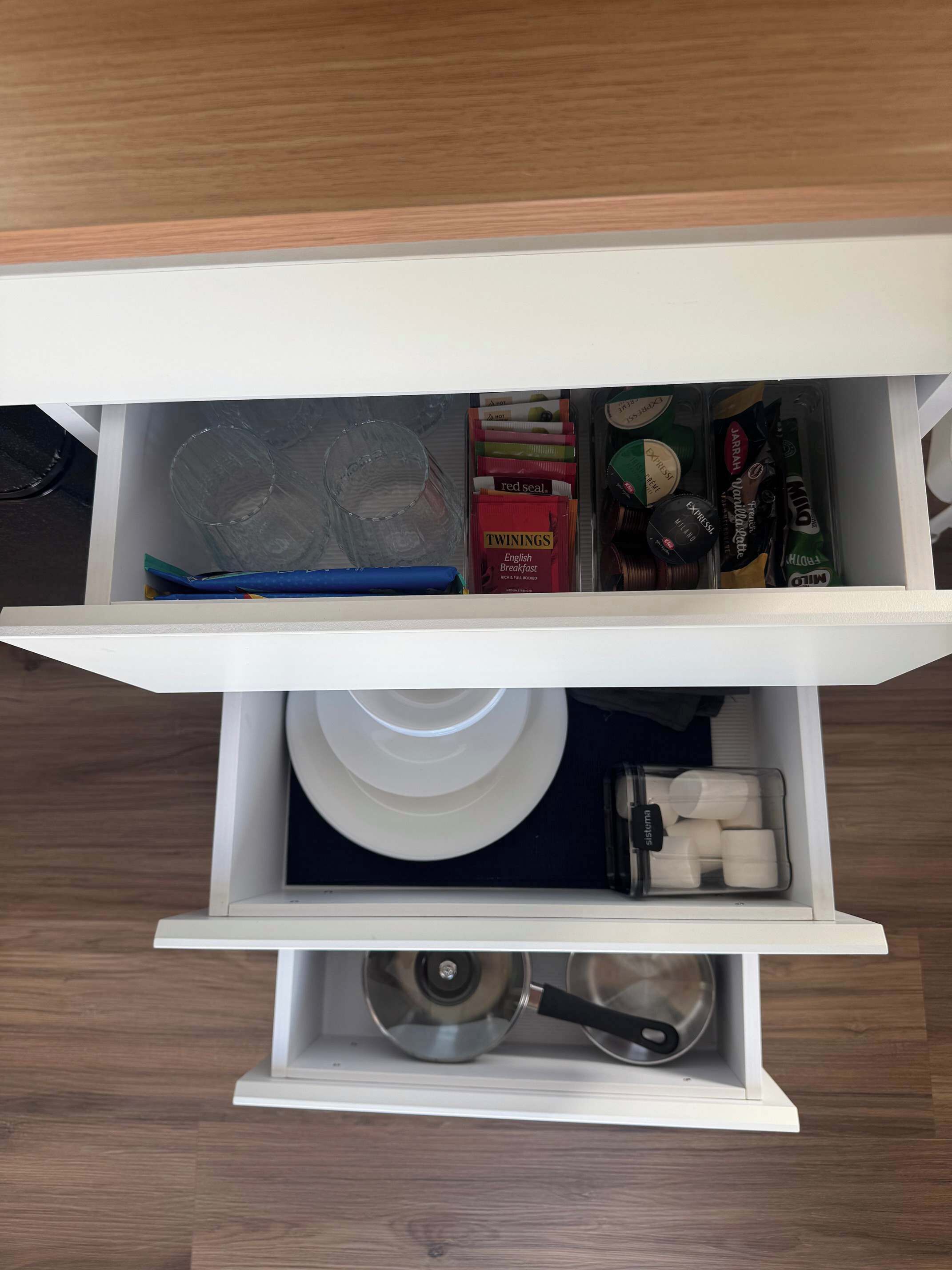 Un tiroir de cuisine contenant divers objets, notamment une assiette blanche, une casserole et des emballages alimentaires.