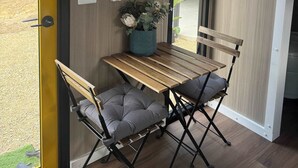 Een kamer met een houten tafel, twee comfortabele stoelen, een potplant, een kunstwerk in een lijst en een gele deur.