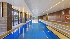 Ein moderner, überdachter Schwimmbereich mit Glaswänden, Holzvertäfelung und heller Decke.