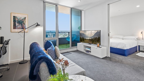 Ein modernes Hotelzimmer mit großem Fenster, einem Bett, einer Couch, einem Fernseher und einem Schreibtisch mit Lampe.