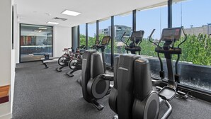 Ein Fitnessraum mit Cardiogeräten, einer Gewichtbank und großen Fenstern mit Blick auf die Stadt.