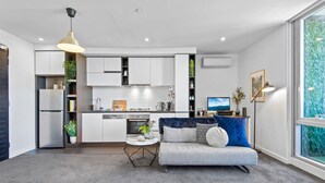 Eine moderne Küche mit weißen Schränken, einem eingebauten Ofen und einem Essbereich mit grauem Sofa und blauen Kissen.