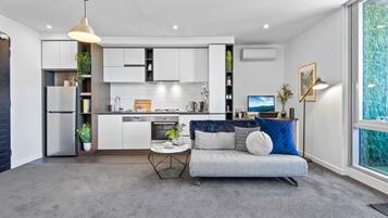 A modern kitchen with white cabinets, a built-in oven, and a dining area with a gray sofa and blue cushions.
