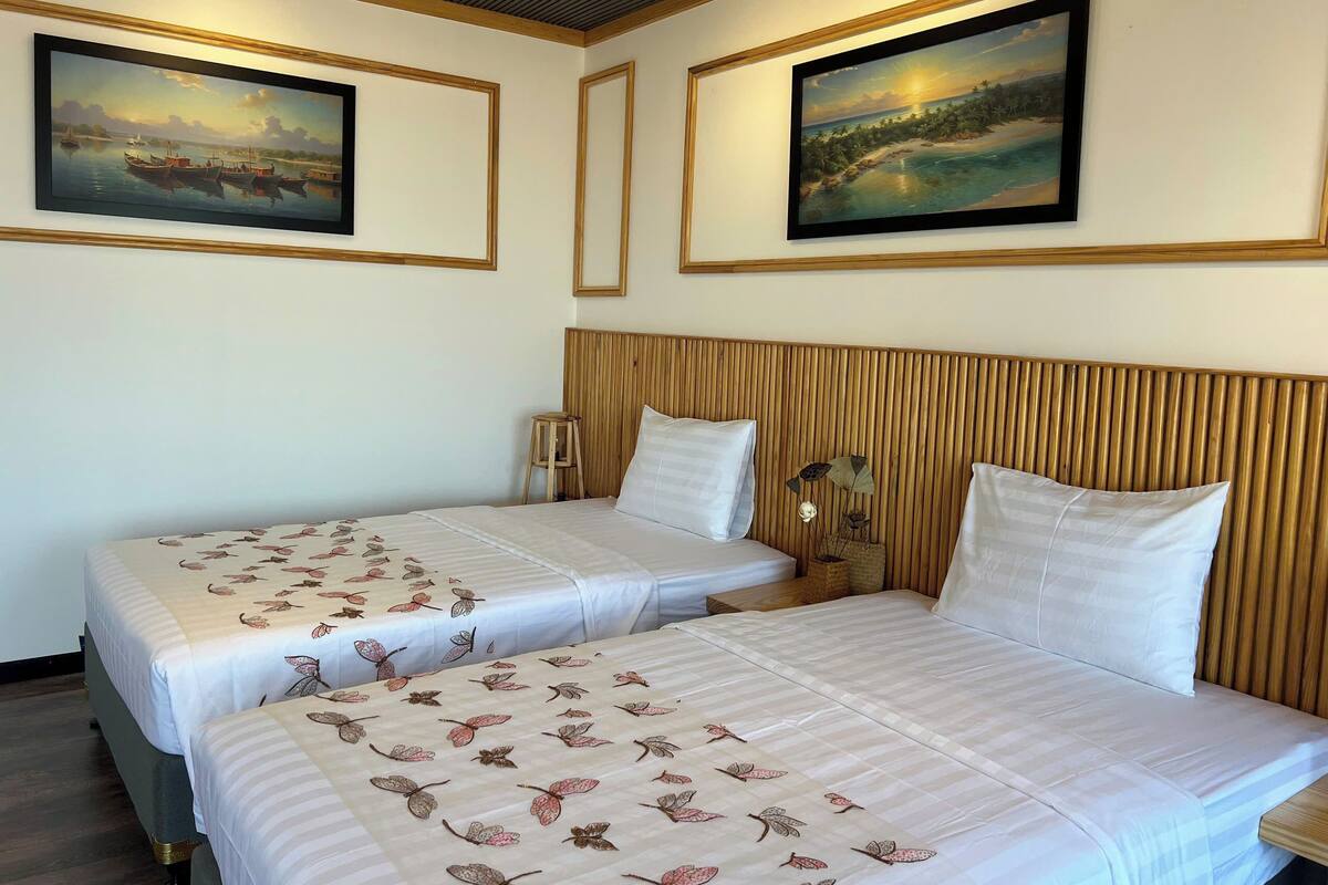A hotel room with two beds, each with a floral bedspread, wooden headboard, and two framed paintings on the walls.