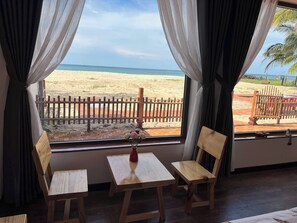 Ein Zimmer mit Holztisch und -stühlen, einem Fenster mit Blick auf einen Strand und einen Holzzaun.