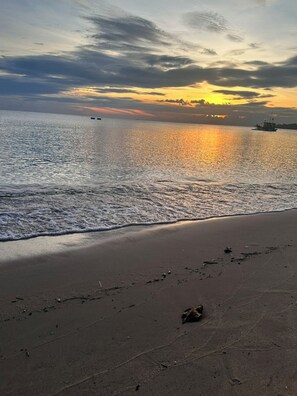 Ein Strand mit ruhiger See, ein Boot in der Ferne und ein Sonnenuntergang im Hintergrund.