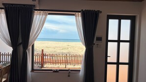 A room with a large window, a wooden door, and a view of a beach.