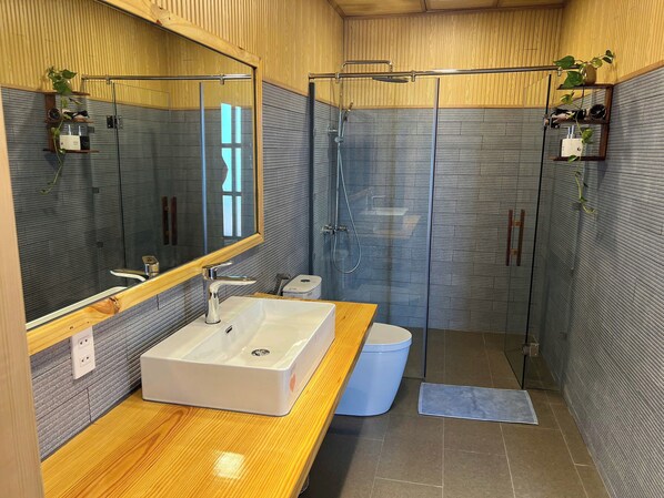 Une salle de bain moderne avec un meuble-lavabo en bois, un grand miroir, une cabine de douche en verre et une petite poubelle.
