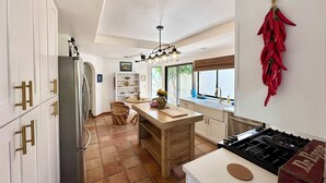 Una cocina moderna con armarios blancos, una isla central, una estufa y una decoración de chile rojo colgante.