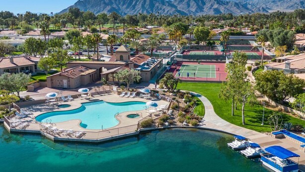 Vista aérea de un complejo turístico con una gran piscina, canchas de tenis y vistas a la montaña.
