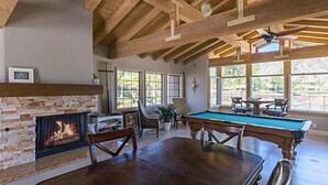 Una habitación amplia con mesa de billar, chimenea y grandes ventanales con vistas al exterior.