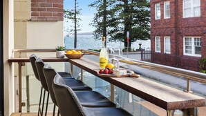 A balcony with a wooden table, black chairs, and a view of the sea. - Manly Muse with Water View and Lock Up Garage (Manly)