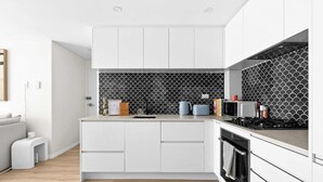 A modern kitchen with white cabinetry, a black and white tiled backsplash, a built-in oven, and a microwave. - Manly Muse with Water View and Lock Up Garage (Manly)