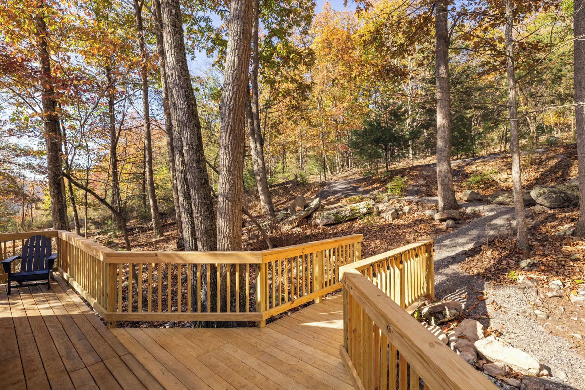 A wooden deck with a railing, surrounded by trees and a rocky path.