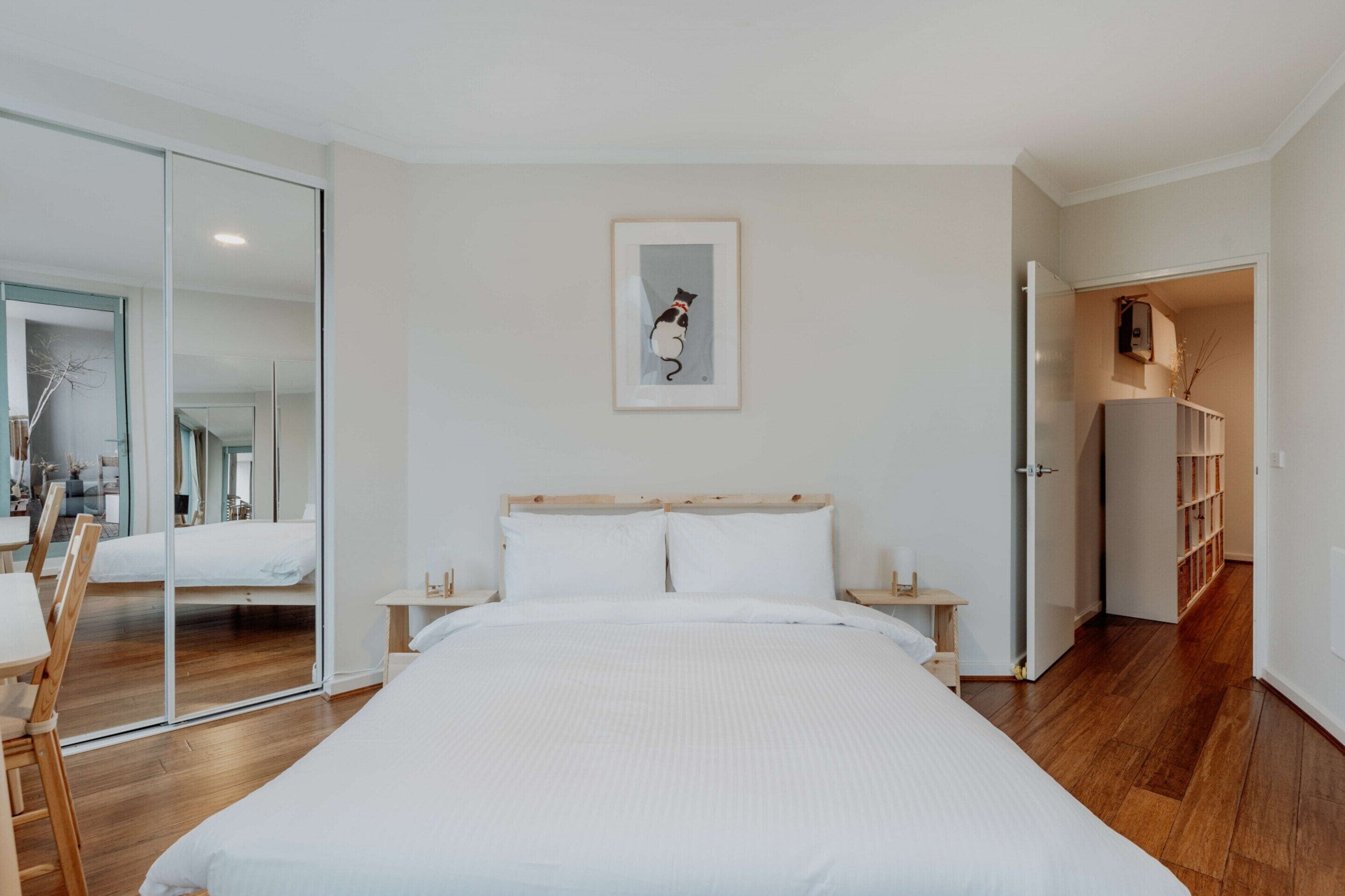 A modern bedroom with a large bed, a glass door leading to a balcony, and a wooden floor.