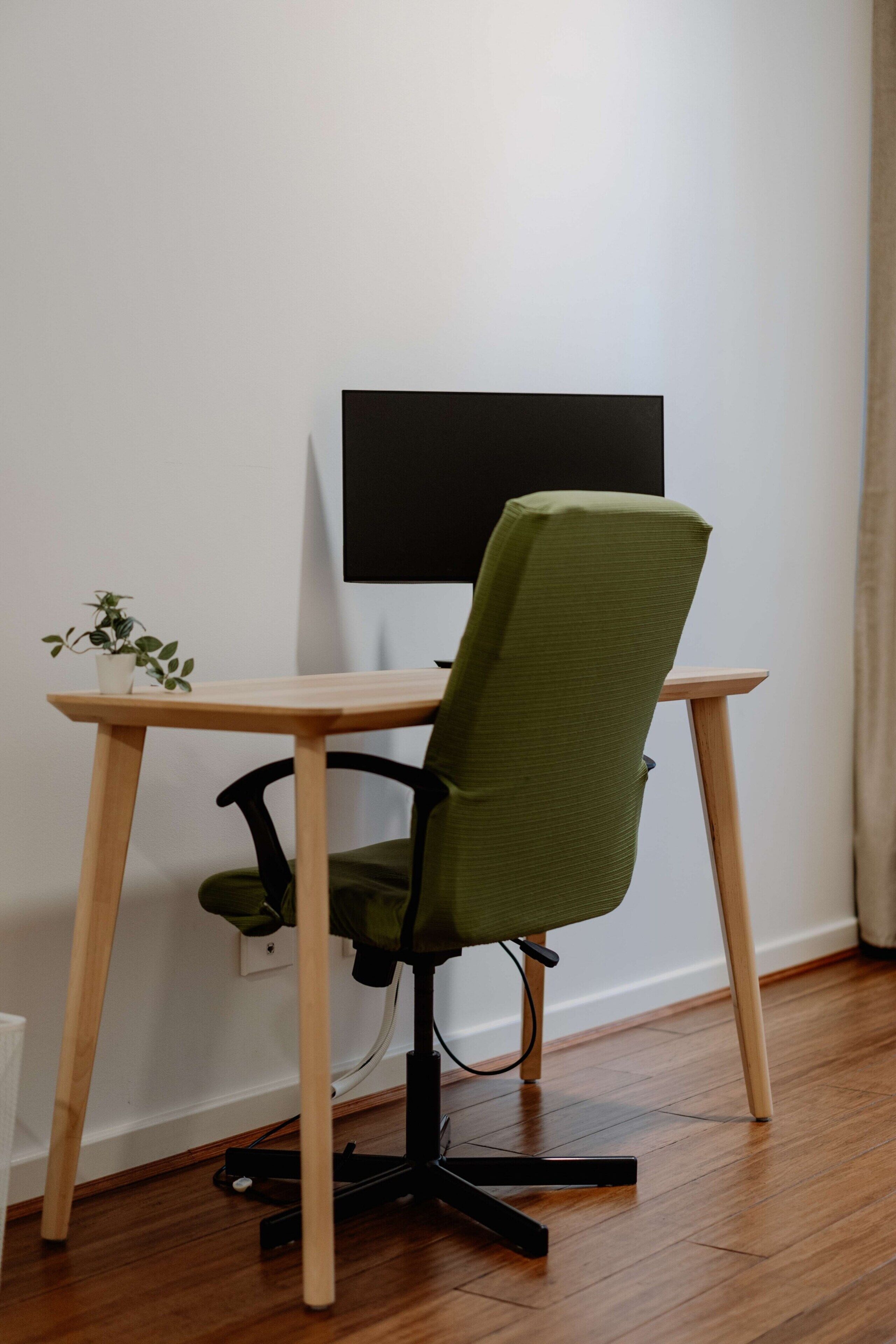 Un espace de travail avec une chaise verte, un bureau en bois et un écran noir.