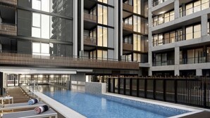 A modern building with a large indoor swimming pool, multiple balconies, and wooden deck areas. - Chic 1-bed With City Views, Parking, Gym & Pool (Melbourne)