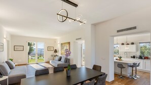 Ein modernes Wohnzimmer mit einem großen Esstisch, grauen Sofas und Blick ins Freie.