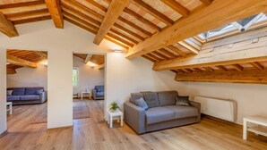 Ein geräumiges Loft mit freiliegenden Holzbalken, einem grauen Sofa und einem kleinen weißen Tisch.