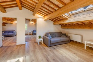 Ein geräumiges Loft mit freiliegenden Holzbalken, einem grauen Sofa und einem kleinen weißen Tisch.