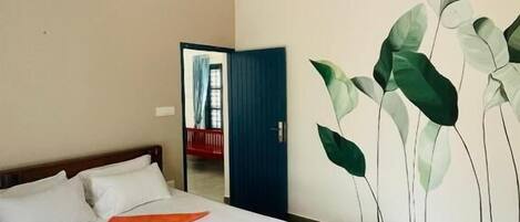 A bedroom with a bed, a ceiling fan, a wall with a plant mural, and a door leading to another room.