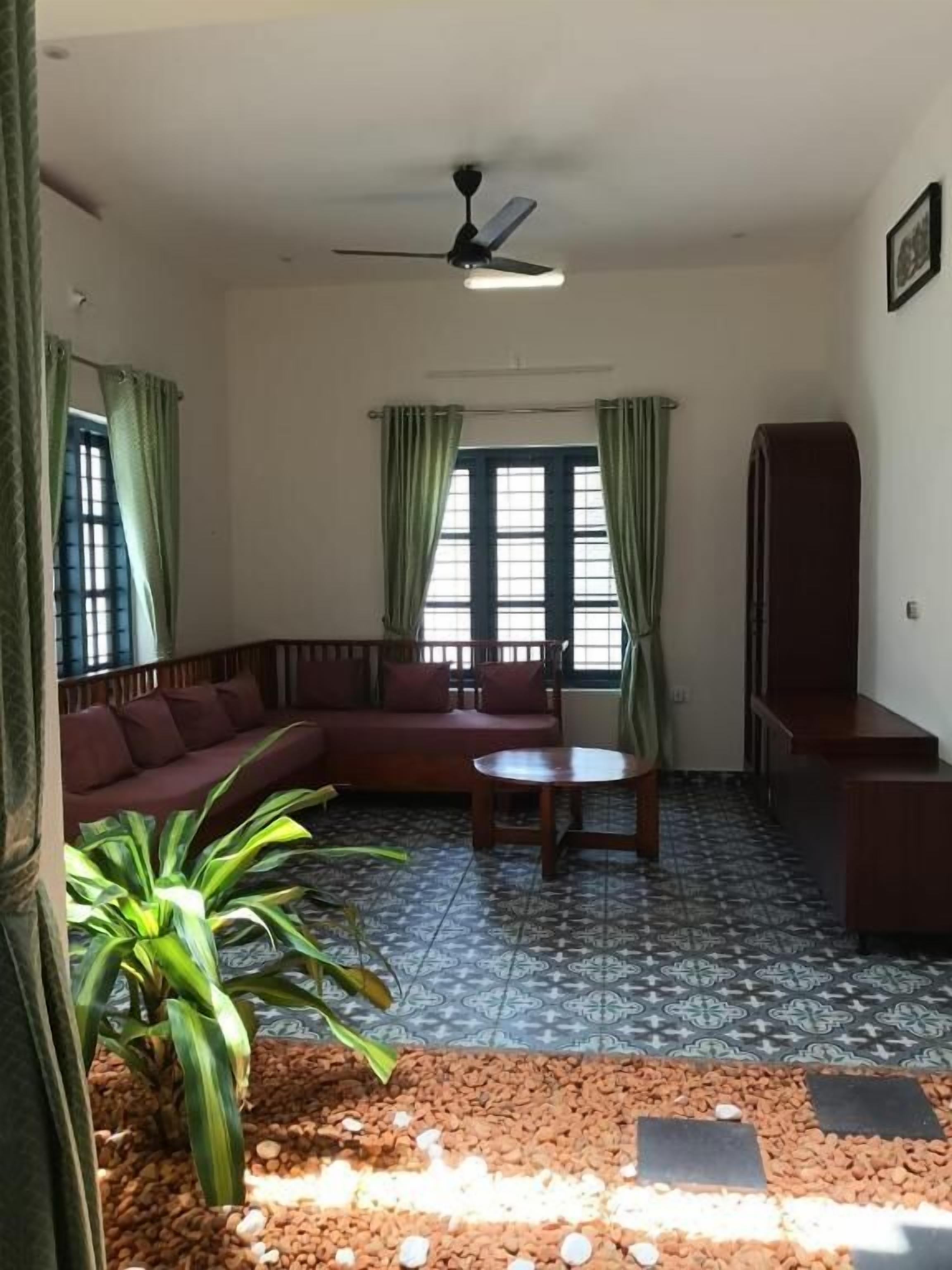 A living room with a sofa, a small table, a ceiling fan, and a window with curtains.