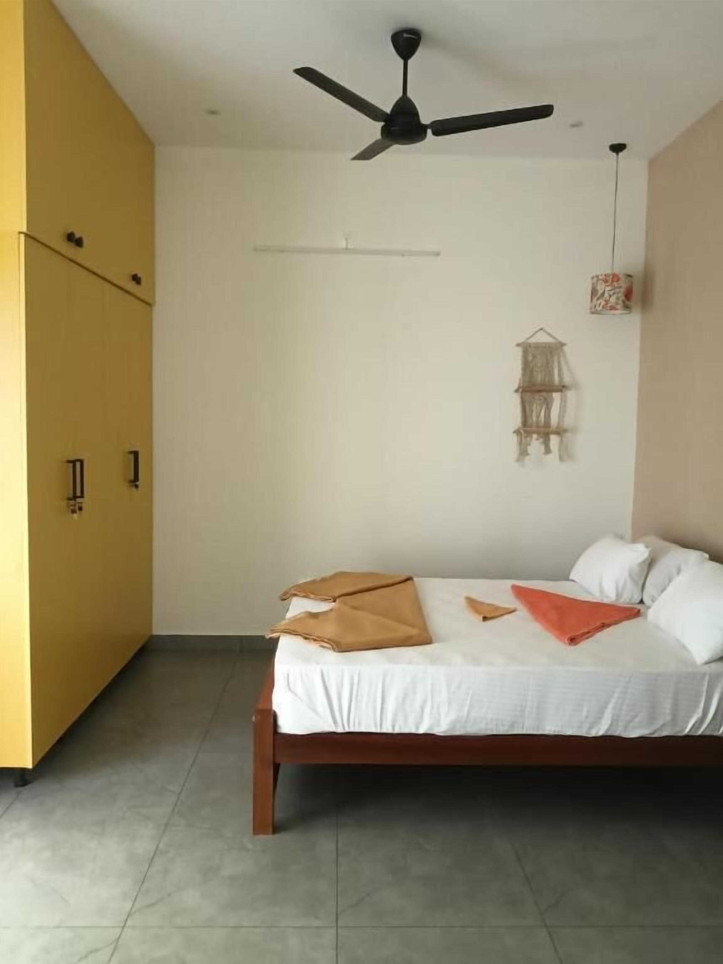 A bedroom with a bed, a ceiling fan, a wall-mounted shelf, and a door.