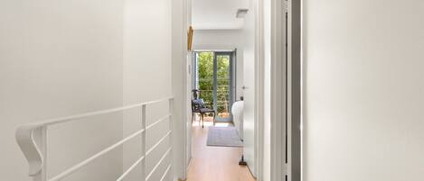 A narrow hallway with a wooden floor, white walls, and a white railing.