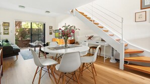 A modern living room with a dining area, a staircase, and a view of the outdoors. - Spacious 2-bed Townhouse With a Lush Courtyard (Sydney)