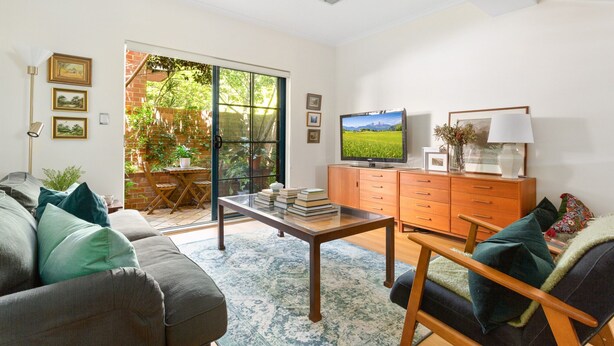 A living room with a sofa, a coffee table, a TV, and a sliding glass door leading to a garden. - Spacious 2-bed Townhouse With a Lush Courtyard (Sydney)