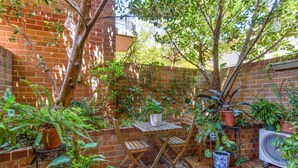 A patio with a brick wall, potted plants, a wooden table, and chairs. - Spacious 2-bed Townhouse With a Lush Courtyard (Sydney)