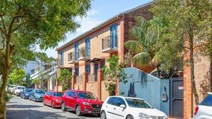 A street lined with parked cars and a row of brick buildings with balconies. - Spacious 2-bed Townhouse With a Lush Courtyard (Sydney)