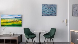 Une pièce avec une table ronde, deux chaises vertes, un tableau représentant un paysage et un buffet.
