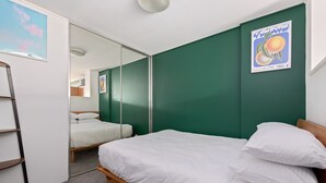 Une chambre avec un lit, un miroir, une échelle et un mur vert.