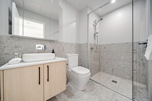 A modern bathroom with a glass-enclosed shower, a white sink, and a toilet.