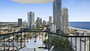 A balcony with a table and chairs, overlooking a cityscape with tall buildings and a beach. - Ocean View 2-bed Studio In the Heart of Surfers (Gold Coast)