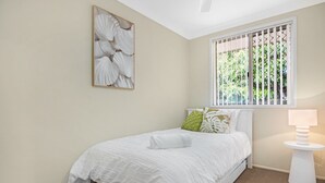 Ein Schlafzimmer mit Bett, einem Fenster mit Gitterstäben, einer Nachttischlampe und einem an der Wand befestigten Kunstwerk.