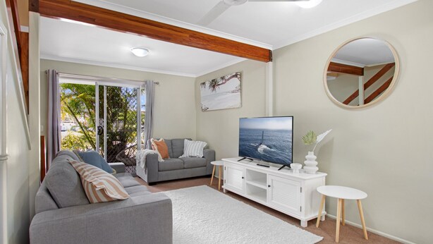 Ein modernes Wohnzimmer mit einem grauen Sofa, einem weißen Couchtisch und einem Flachbildfernseher auf einer weißen Kommode.