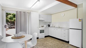 Eine moderne Küche mit weißen Schränken, einem Kühlschrank, einer Mikrowelle und einem Herd. Ein Esstisch mit Stühlen und ein Fenster mit Vorhängen sind ebenfalls vorhanden.