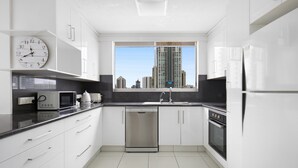 Eine moderne Küche mit weißen Schränken, einem Edelstahl-Geschirrspüler, einem Einbauofen und einem großen Fenster mit Blick auf die Stadt.
