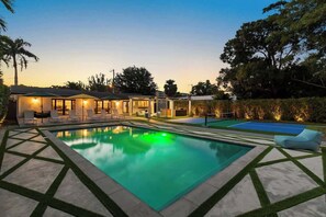 A modern outdoor pool area with a rectangular pool, lounge chairs, and a covered seating area.