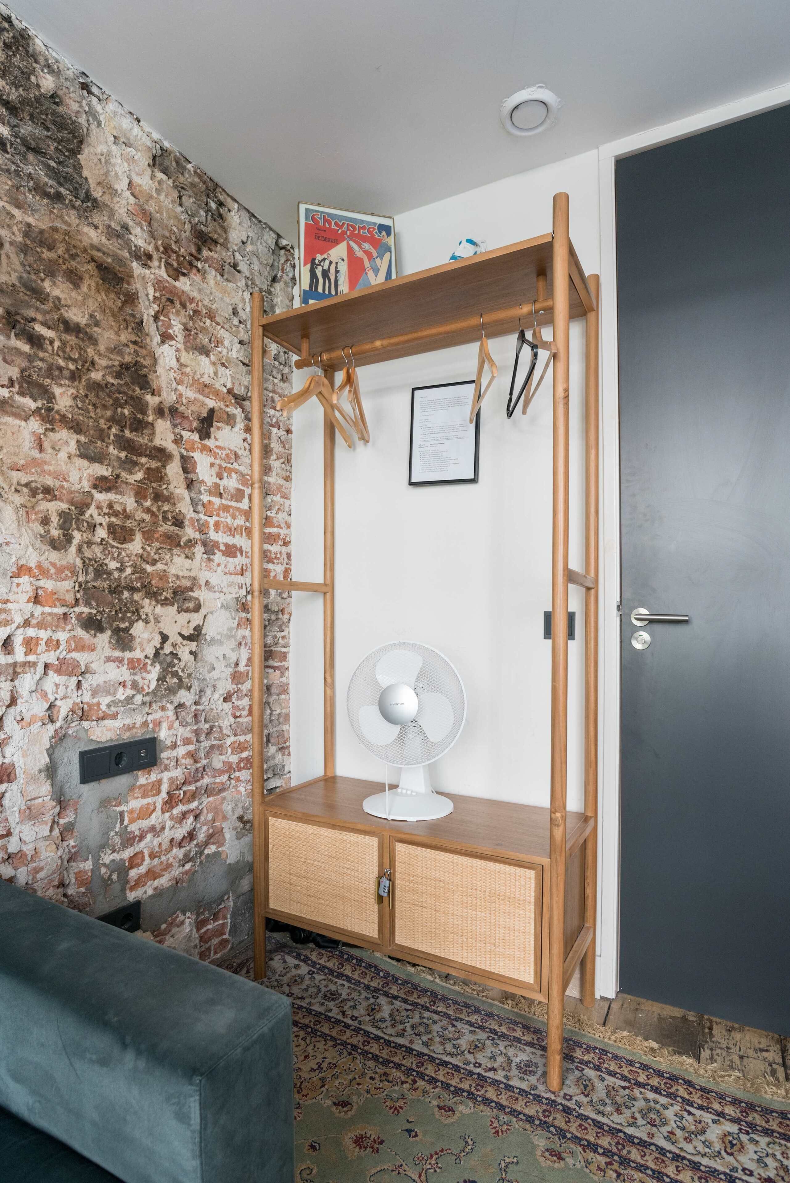Een kamer met een bakstenen muur, een houten garderobe, een witte ventilator en een kamerbreed tapijt met een patroon.