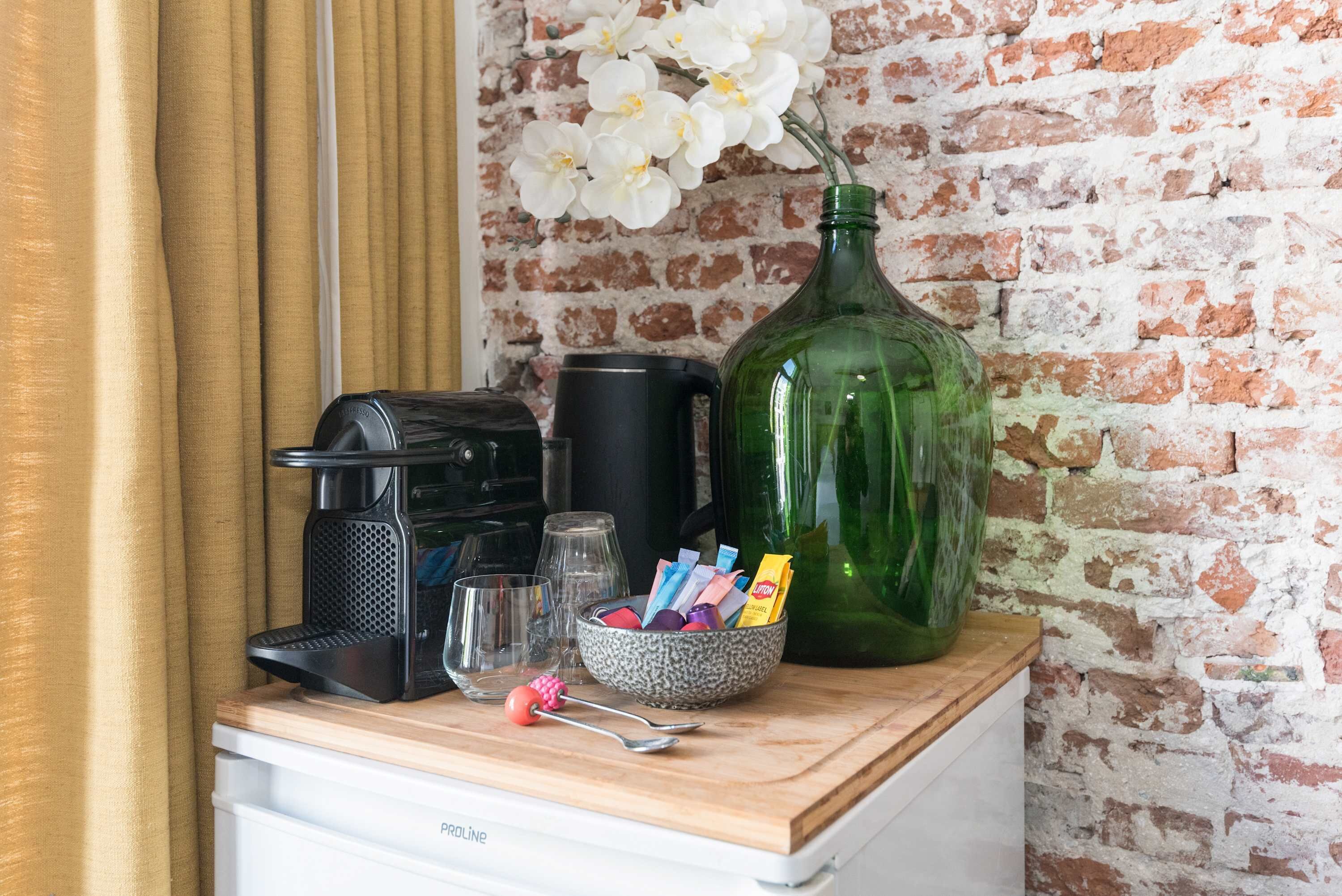 Een aanrecht met een koffiezetapparaat, een groene fles, een schaal met snacks en een lepel.