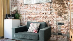 A room with a brick wall, a grey sofa with a floral pillow, a small white cabinet, and a patterned rug.